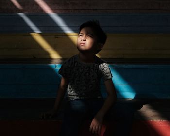 Thoughtful boy looking away while sitting on bench