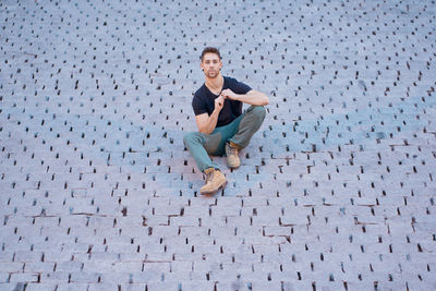 Drontal view of a modern man in casual clothes sitting on some cobbles