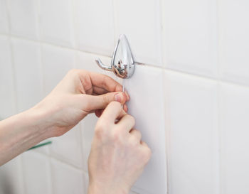 The hands caucasian guy are tightening a screw with a hex wrench from a small metal hanger on a wall