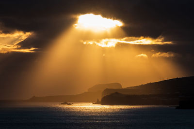 Sunlight streaming through clouds over sea during sunset