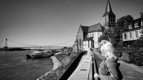 Woman sitting on bridge over river against sky