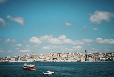 Sailboats in sea by buildings in city against sky