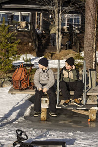 Full length of boys sitting together on jetty during sunny day