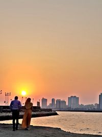 People on sea by cityscape against sky during sunset