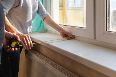 Young couple moving in new apartmen. people measure size of window sill with a tape measure. 