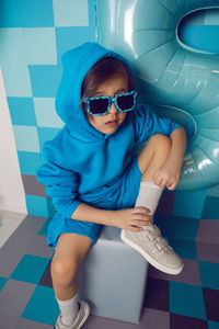 Boy child in blue clothes and a cap is sitting on a gray square celebrating his birthday.