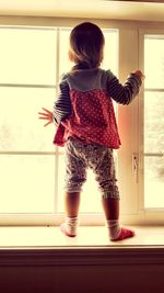 Rear view full length of baby girl standing by window at home