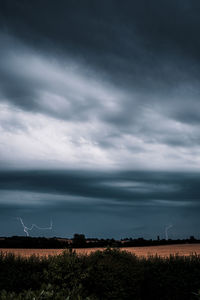 Scenic view of field against cloudy sky with lightning