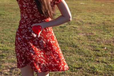 Midsection of woman holding red while standing on field