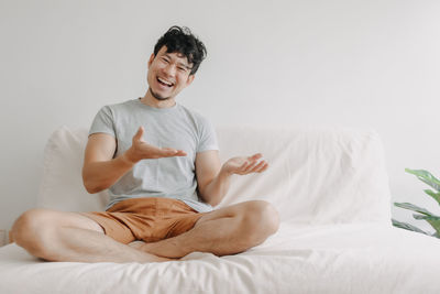 Portrait of smiling man gesturing sitting on bed at home