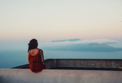 Rear view of woman looking at sea against sky during sunset