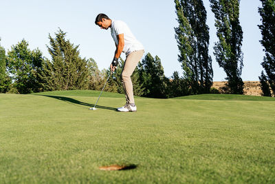 Professional male golf player preparing to hit ball with putter in green field while looking down on summer day