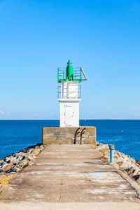 Lighthouse by sea against clear blue sky