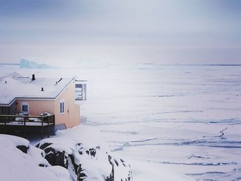 Snow covered houses by sea against sky