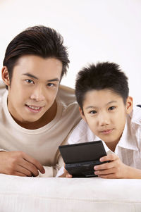 Father and son using mobile phone against wall at home