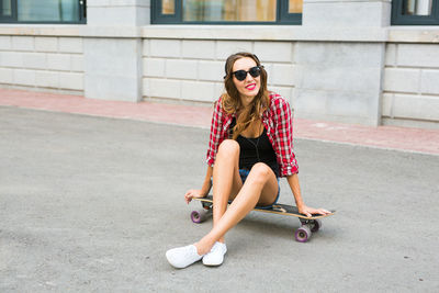 Portrait of young woman sitting on skateboard