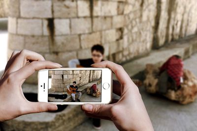 Cropped hands photographing boy playing guitar against wall