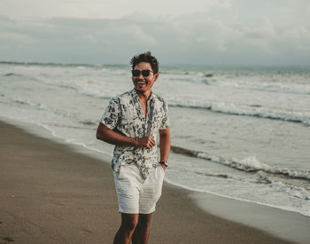 Full length portrait of smiling man standing on beach