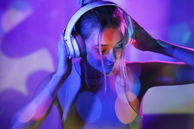 Woman listening to music wearing headphones in front of wall