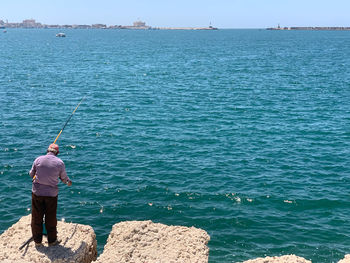 Rear view of man standing on rock by sea