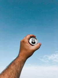 Cropped hand holding a tin against blue sky