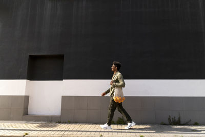 Man with bag of oranges walking on footpath during sunny day