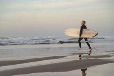 Full length of man with surfboard at beach against sky