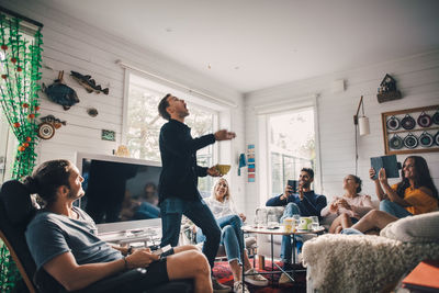 Friends photographing man throwing food while standing in living room at home