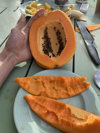 Close-up of hand holding papaya fruit in plate on table