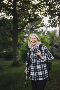 Portrait of happy senior woman holding hiking poles while hiking in forest