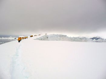 People walking on snow covered landscape against sky at antarctica