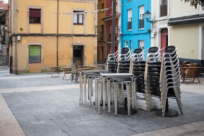 Empty chairs on sidewalk by buildings in city