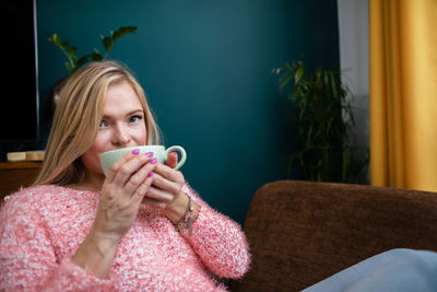 A young woman drinks coffee while sitting in the living room.