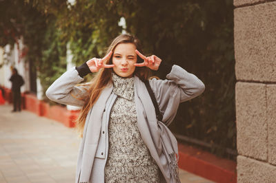 Portrait of young woman gesturing while standing in city