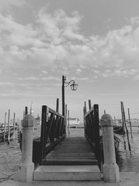 Wooden pier on sea against cloudy sky