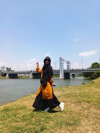 Young woman standing on riverbank against sky