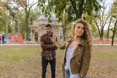 Woman gesturing stop sign to man against trees