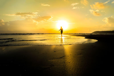 Silhouette man standing on beach against sky during sunset