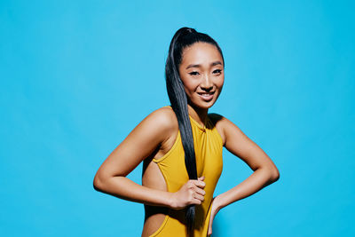 Portrait of young woman standing against blue background