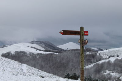 Road sign on snowcapped mountain against sky