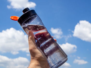 Hand holding glass bottle against sky