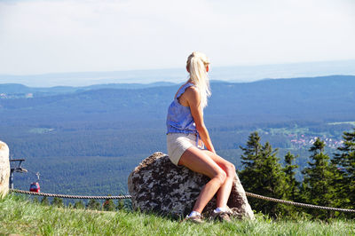 Woman sitting on rock against sky