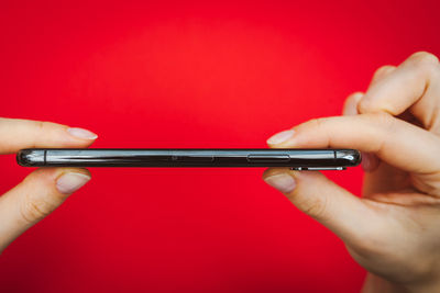 Cropped image of hands holding mobile phone against red background