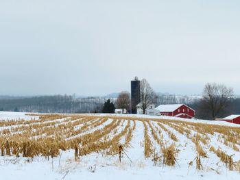 Snow covered field with red barn and silos against sky