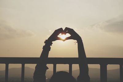 Silhouette person standing by heart shape against sky during sunset