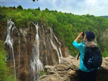 Rear view of woman photographing waterfall at plitvice lakes national park