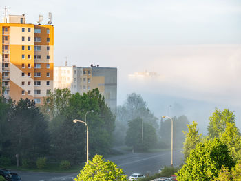 Flat houses and trees on the hill above morning mist. cars waiting on parking place