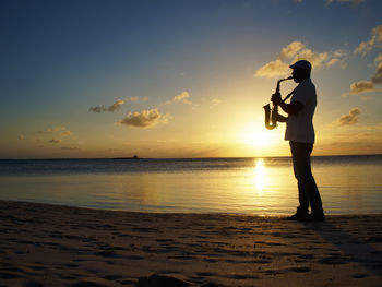 Silhouette man standing on beach against sky during sunset