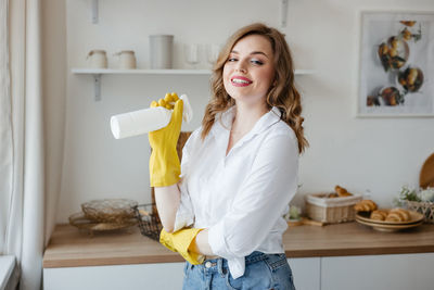 A girl in yellow gloves holds a cleaning spray on the background of the kitchen