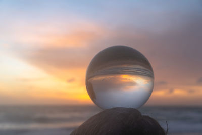 Close-up of crystal ball against sea during sunset